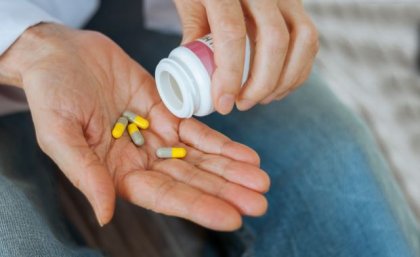 A close up photo of a hand pouring yellow and brown tablets from a white plastic pill bottle onto an open palm.